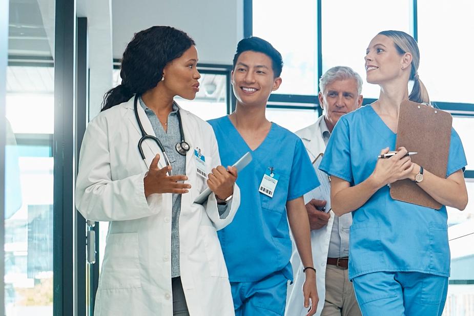 Group of people in scrubs and lab coats, walking around a hospital while they chat.